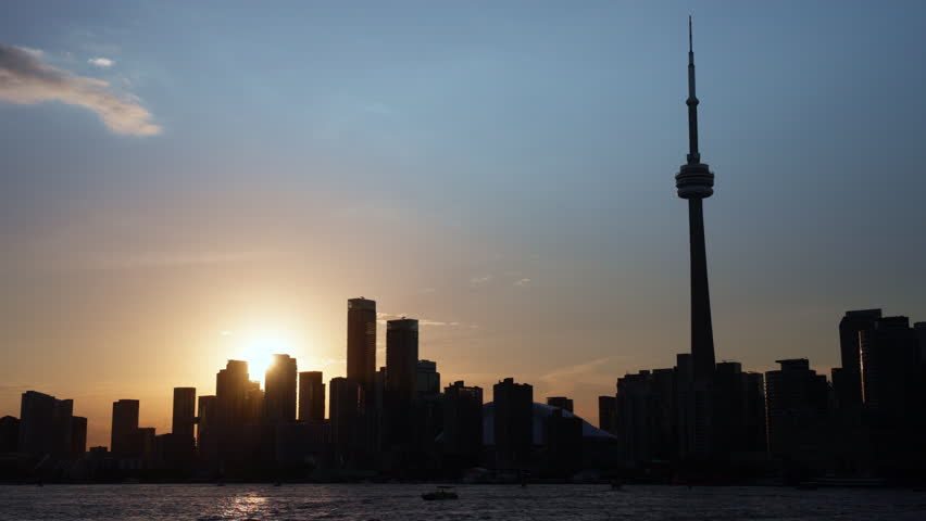 Toronto skyline and CN Tower viewed from a moving boat as the sun sets behind the city with reflections on the water, Slow Motion