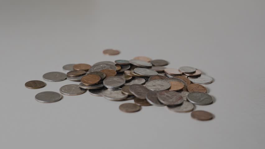 Loose American coins, including quarters, dimes, nickels, and pennies, dropping and scattering on a white surface, showcasing financial concepts like savings and wealth accumulation with dynamic motion.