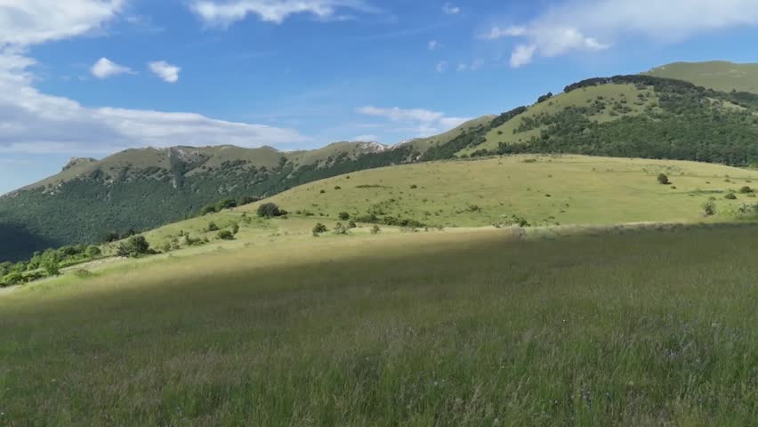 Mountain landscape with overlapping ridges illuminated by sunbeams filtering through the clouds, green meadow in the foreground and deep and bright natural atmosphere