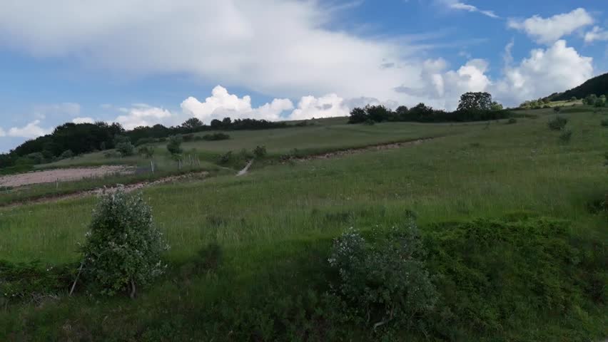 Wide landscape with green meadows, cultivated hills, under a blue sky with white clouds