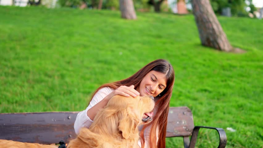 Happy young woman receiving kisses and cuddles from her loving pet dog in a beautiful green park