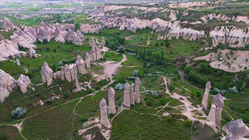 drone view showing the extensive layout of Love Valley fairy chimneys amidst green vegetation fields. Spectacular geological nature landscape in Cappadocia, Turkey