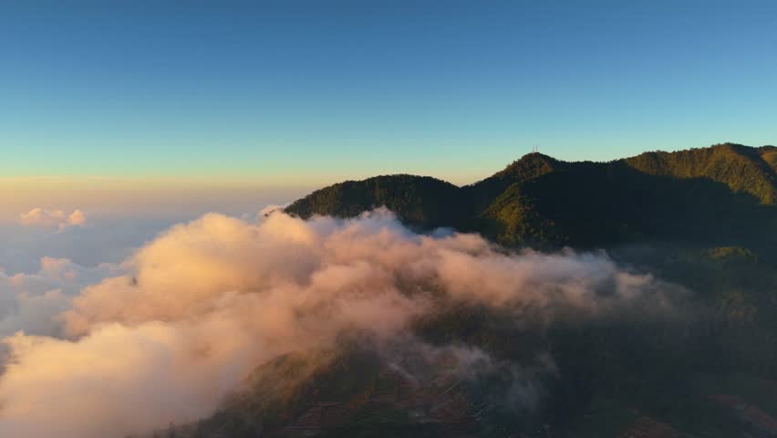 Aerial view of Bukit Skoter mountain peak rising above a thick sea of clouds during golden hour in Kecamatan Batur, Jawa Tengah, Indonesia.