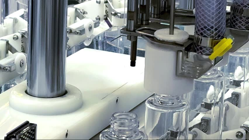 Industrial automated machinery line handling clear cosmetic serum bottles in manufacturing plant	