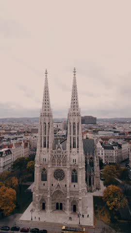 Aerial view of an impressive cathedral featuring twin spires, surrounded by a vibrant city landscape, showcasing architectural beauty in Vienna at the Votivkirche church in vertical video format.