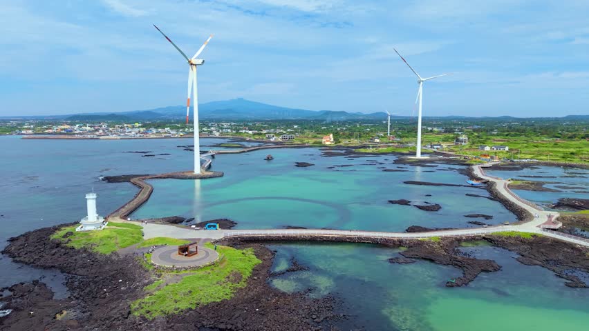 Aerial sideways of Sinchang Lighthouse wind turbines and volcanic rocky coastline at Singgyemul Park, Sinchang-ri, Jeju island