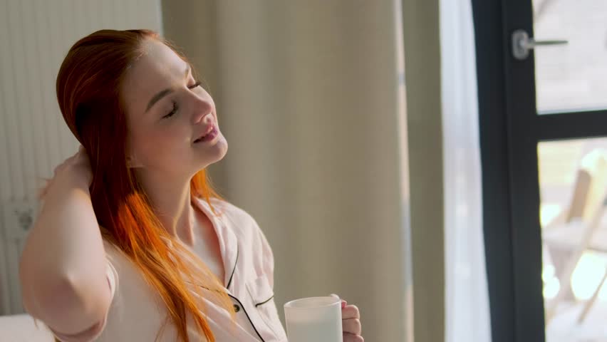 Close up portrait of a beautiful young redhead woman holding a coffee mug and enjoying a peaceful morning.