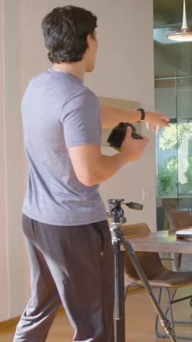 Vertical video: Entering dining room, man in grey tee shooting wall art with DSLR, capturing angles. Photography, interior, sunlight, tripod, camera, framing, vertical video