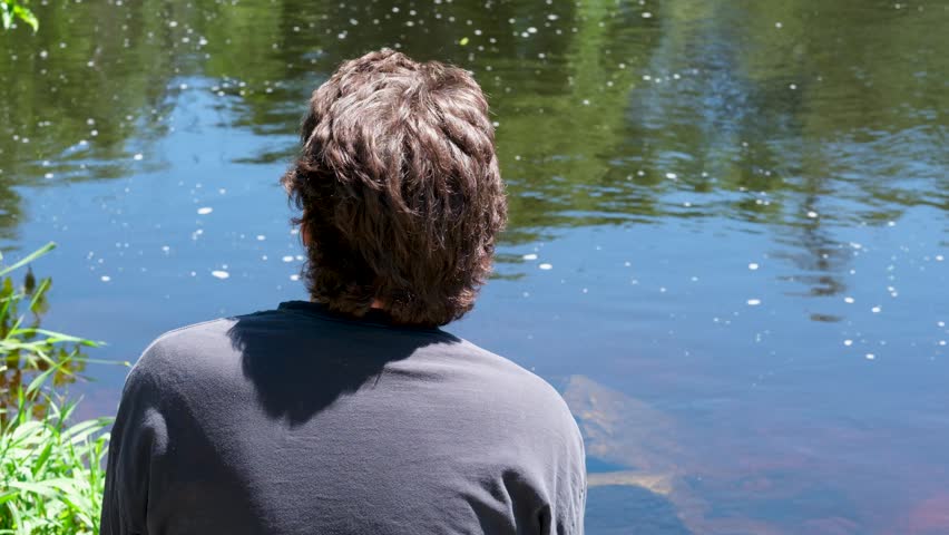 Man Sitting on Riverbank Enjoying Peaceful Nature View