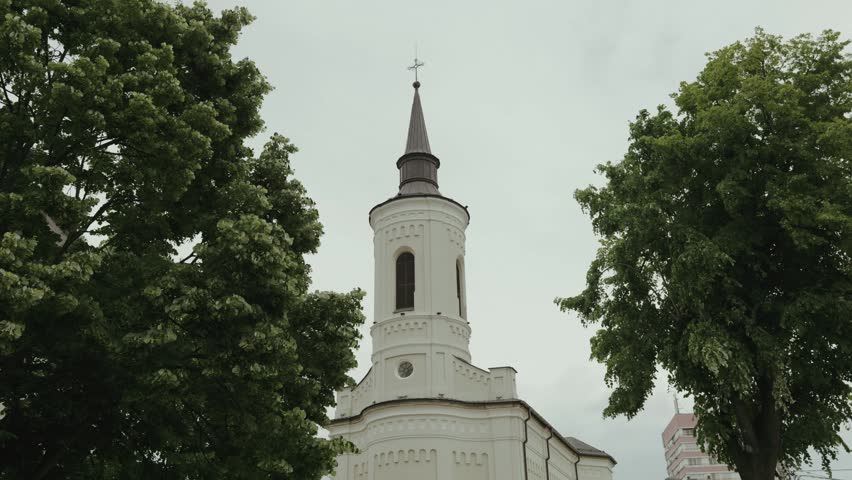 Scenic view of a historic white Christian church tower surrounded by blooming trees and lush greenery. European landmark from Iasi city, Romania.