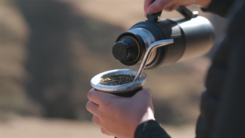 Hot water poured into a yerba mate gourd outdoors in Argentina, featuring traditional preparation, social customs and South American beverage culture, close-up shot.