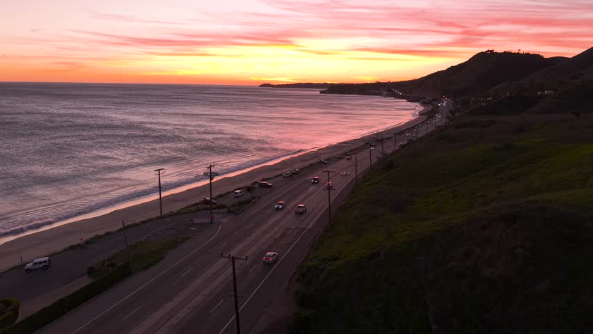Gorgeous Sunset on Malibu coastline at dusk, Pacific Coast Highway tracing the California shore as warm evening colors fill the dramatic horizon. PCH Highway traffic cruises by