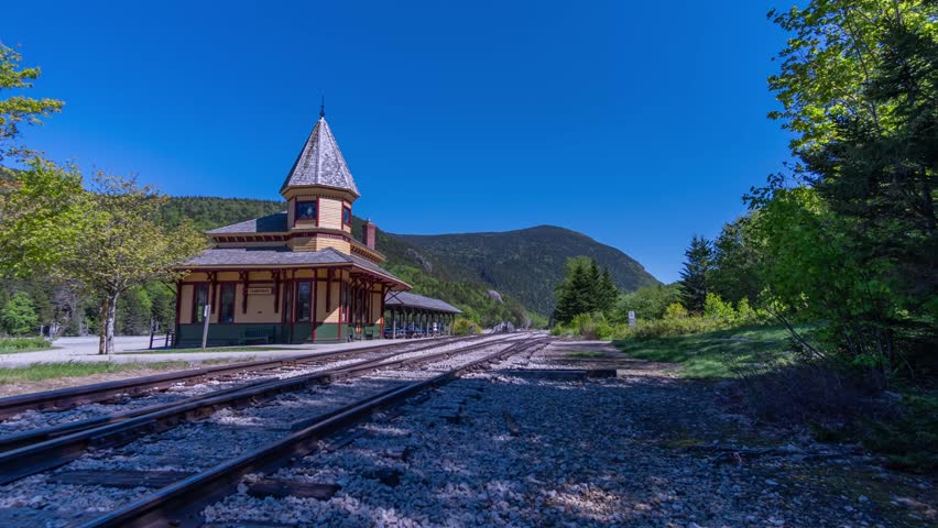 Time-lapse shot of the Crawford Notch Depot stands beside empty railroad tracks under a clear blue sky in White Mountain National Forest, Lincoln, New Hampshire, US