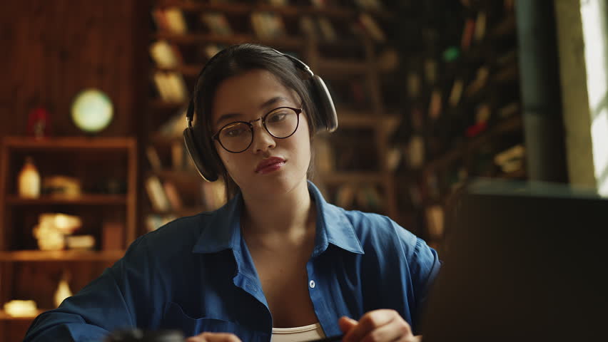 Asian female student in headset answering question during online video lesson