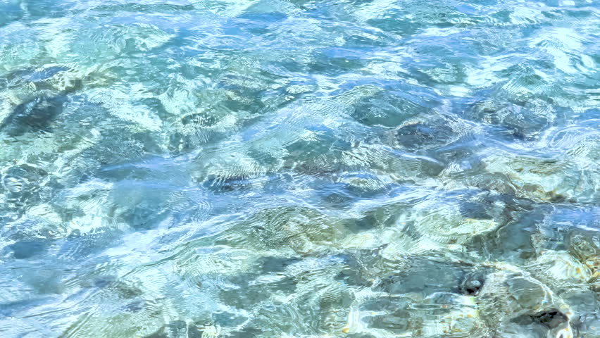 Slow motion view of crystal clear water in Sardinia showing turquoise sea surface, gentle waves and natural Mediterranean sunlight reflections.