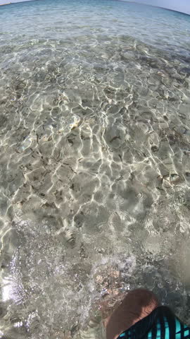 Vertical POV slow motion walk in crystal clear Sardinian sea showing legs and feet underwater in turquoise water with natural Mediterranean light.