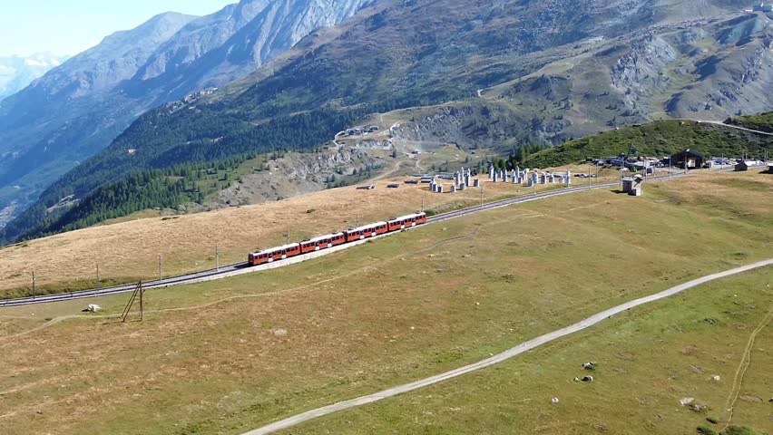 Aerial view of a red train traveling along the mountain tracks through the alpine landscape near Zermatt, Valais, Switzerland.
