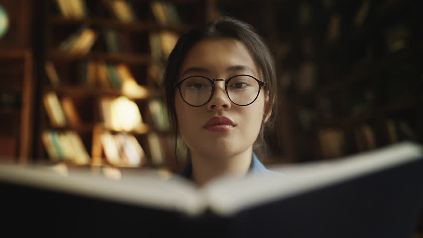 Asian woman in glasses studying medical literature in university library