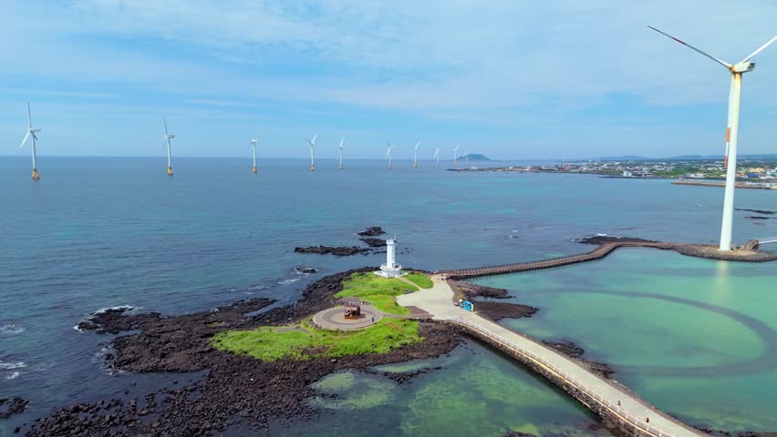 Aerial view of wind turbines, Sinchang Lighthouse and offshore wind farm along Jeju Island coastline with Hallasan mountain backdrop
