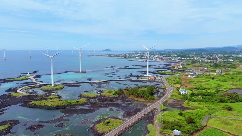 Aerial view of Sinchang costal road wind turbines lining rocky coast and footbridge network at Singgyemul Park Jeju Island
