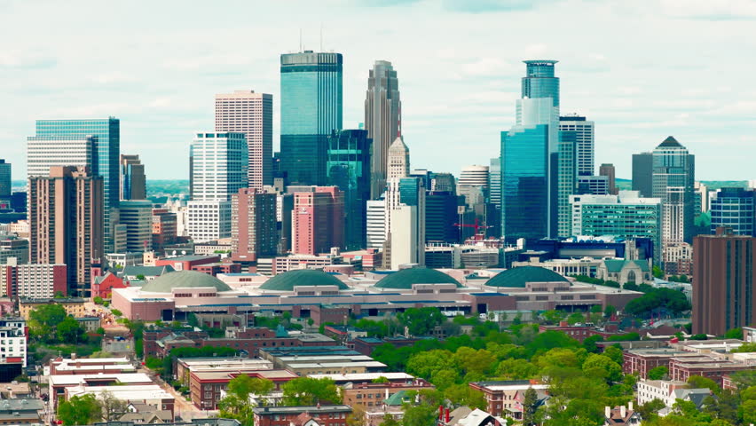 Twin Cities skyline, downtown Minneapolis, Minnesota under a bright sunny sky with skyscrapers above tree-lined city blocks.
