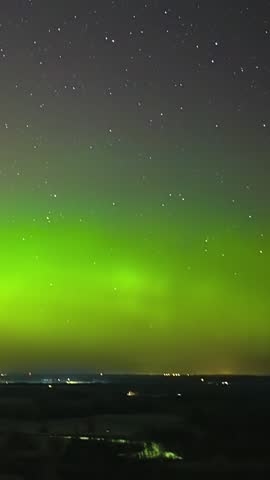 Glowing green yellow pulsing aurora borealis above quiet river valley under starlit sky, vertical time lapse