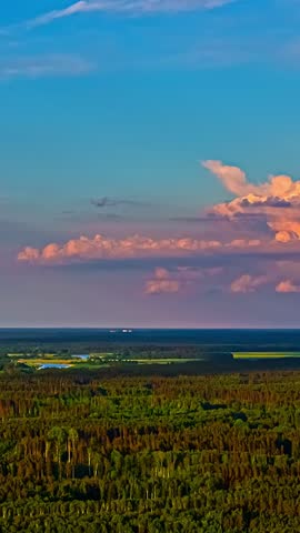 Fast-moving aerial hyperlapse over dense forest and fields under colorful sunset clouds