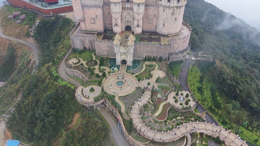 Vietnam, Da Nang, Ba Na Hills Aerial Shot Of Castle Courtyard Fountain, Asian Photographer Framing Ornate Turrets And Winding Stone Paths, Fog Rolling Over Mountain Gardens