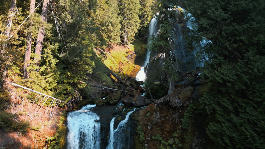 Slow orbital view around Falls Creek Falls upper and lower falls in shaded forest canyon surrounded by rocky surfaces and forest trees