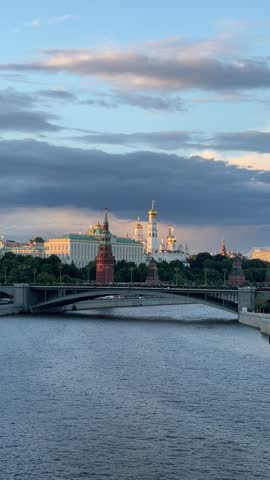 Panoramic view of the Moscow Kremlin and Moskva River at sunset under dramatic storm clouds. Iconic landmarks of Moscow, including the Kremlin towers, cathedrals, and historic embankments, illuminated by soft evening light. Scenic cityscape showcasing Russian architecture, cultural heritage, tourism, travel destination, and urban landscape.