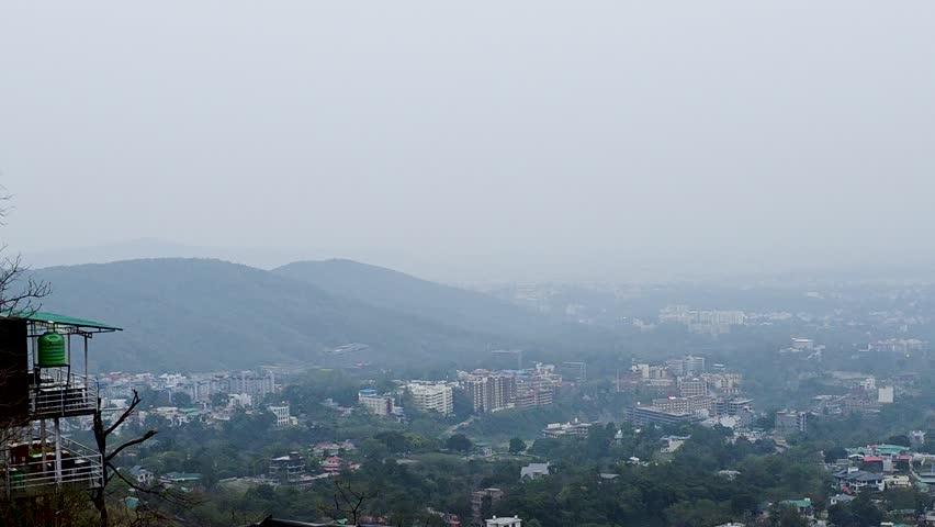 Aerial drone panning shot showing Dehradun town from Mussoorie town at sunset dawn dusk with soft haze fog and all the buildings in the distance surrounded by Himalaya mountains