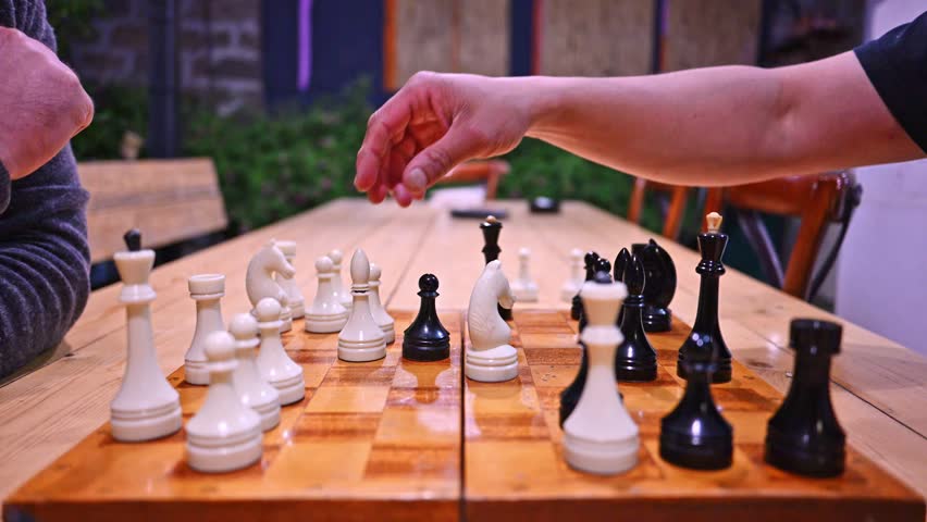Close-up of hands moving chess pieces on wooden board. Two players concentrate during game
