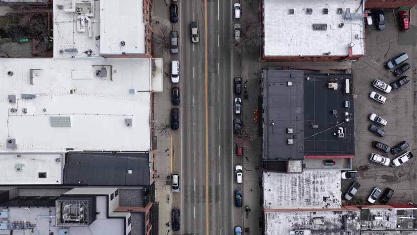 Urban downtown Bozeman with flat commercial rooftops, parked cars, moving traffic and surface parking lots lining main street in Bozeman, Montana, USA. Aerial drone top down flyover