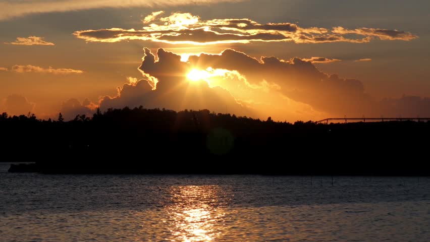 Sunset over calm ocean water with silhouette of bridge and coastline