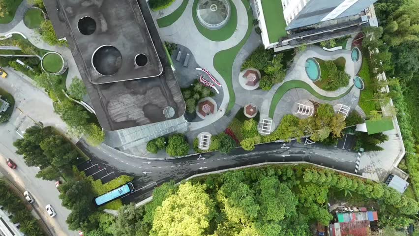 Top down aerial drone view of landscaped courtyard with gazebos and curved walkways beside apartment complex in Malaysia