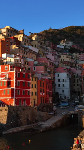 Colorful hillside buildings of Riomaggiore overlook a small harbor at golden hour