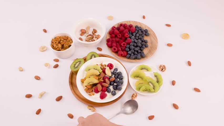 Overhead shot of hand scooping yogurt with fruit and granola from a white bowl.