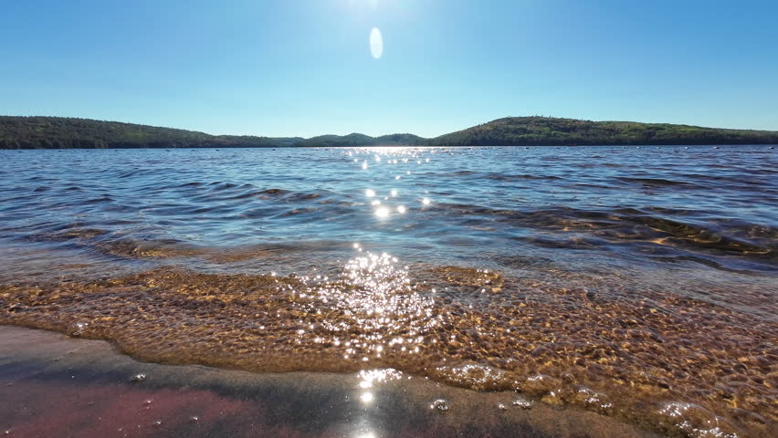 Close view of sunlight reflecting on gentle waves moving toward the sandy shoreline on Grand Lake in Algonquin Provincial Park, Ontario, Canada.