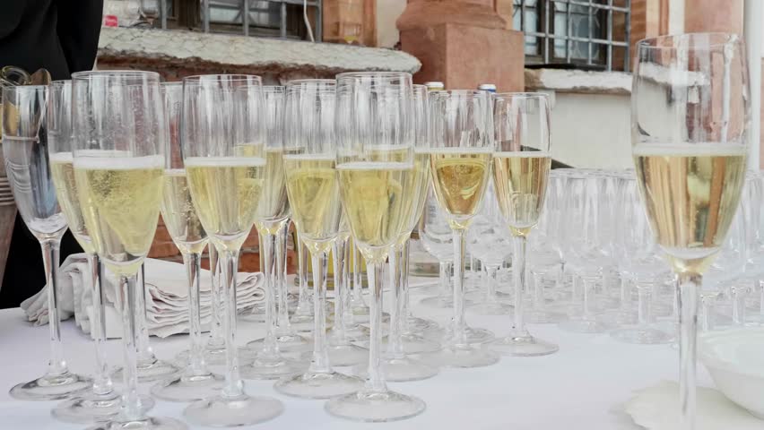 Waiter pouring sparkling wine into rows of elegant glasses on a white tablecloth during a celebration event at an outdoor venue
