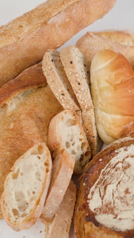 Close-up of hands tearing a flaky croissant over sourdough and baguettes on white background.