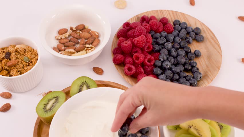 Overhead view of a person arranging fresh berries and fruit into a healthy yogurt bowl.