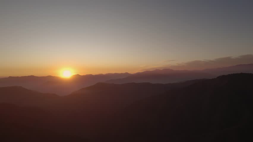 Golden sunrise illuminates distant mountain peaks with a soft gradient sky over Chakrata, Dehradun, Uttarakhand.