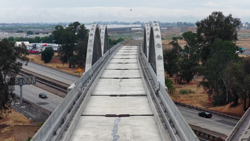 Cedar Viaduct high-speed rail arched bridge deck stretches over dry Central Valley terrain with freeway and agricultural flatlands below in Fresno, California, USA. Aerial drone view.