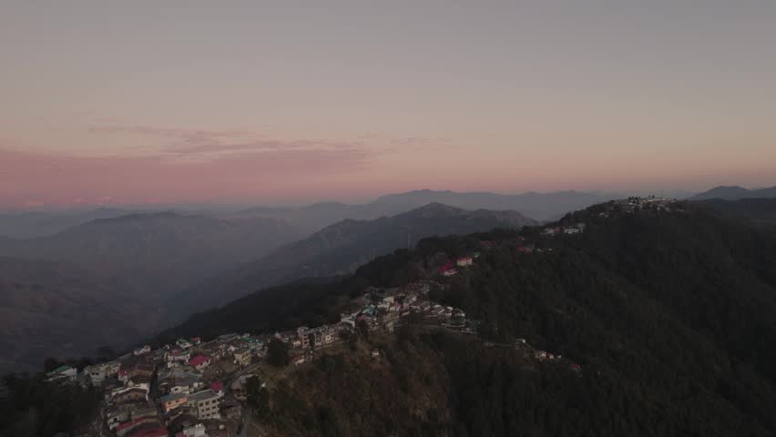 An aerial view captures a village nestled on a mountainside during a soft twilight.