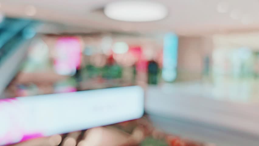 A tranquil view from an elevated point in a bustling modern shopping mall interior, featuring smooth ceilings with evenly spaced circular lights and bright, white floors that reflect ambient light
