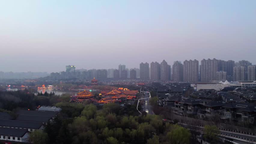 A panoramic urban landscape blending traditional architectural complexes with modern high-rise buildings under a hazy dusk sky.