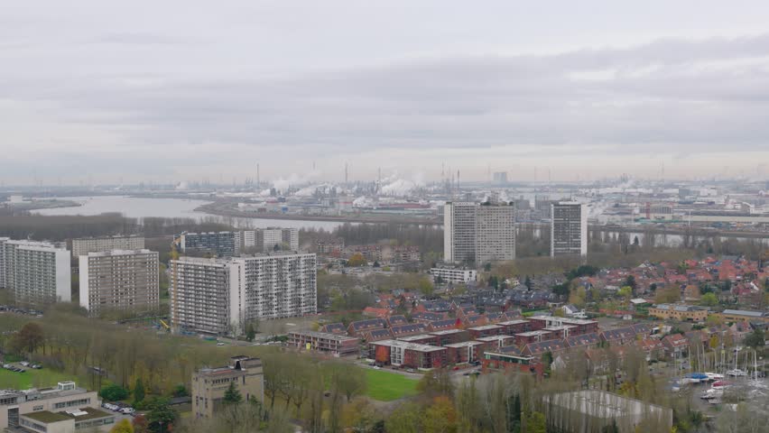 Drone footage from Antwerp’s Left Bank featuring residential towers in the foreground, the Scheldt River, and the Port of Antwerp stretching across the horizon.