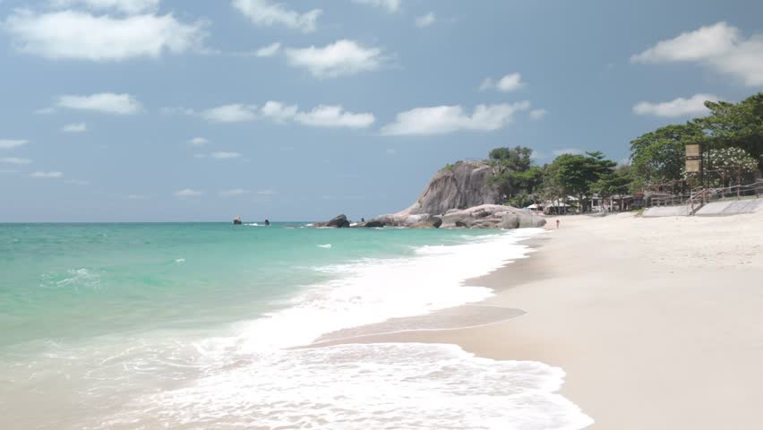 Gentle waves wash onto sandy Lamai Beach with rocky headland and clear sky