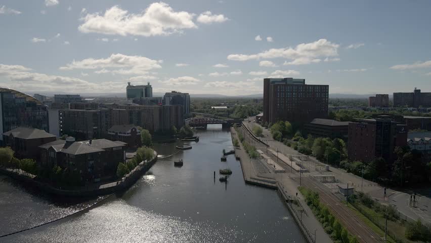 Drone view over Salford Quays capturing contemporary skyline and bridge structure reflected in calm waters. Drone moving forwards over the river towards the metal bridge that crosses it.