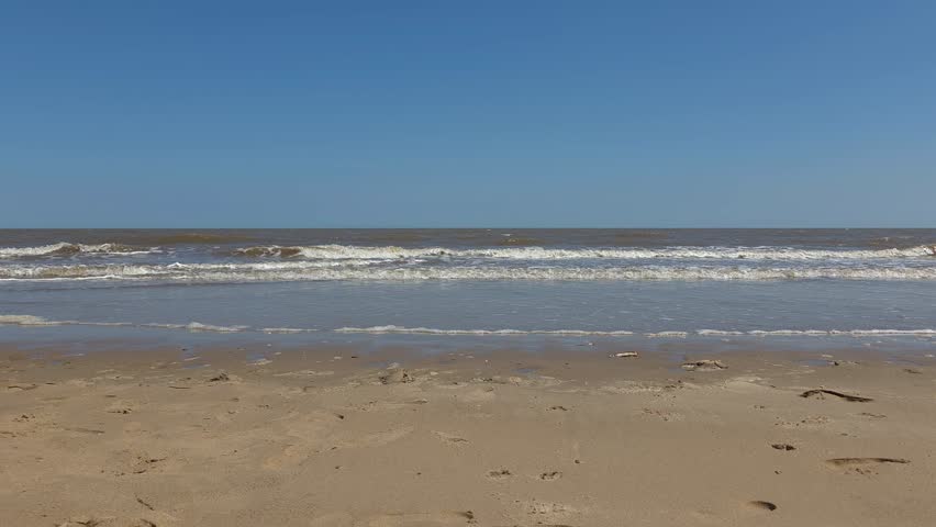 Sandy Beach Shoreline with Muddy Brown Ocean Waves Under Clear Blue Sky
